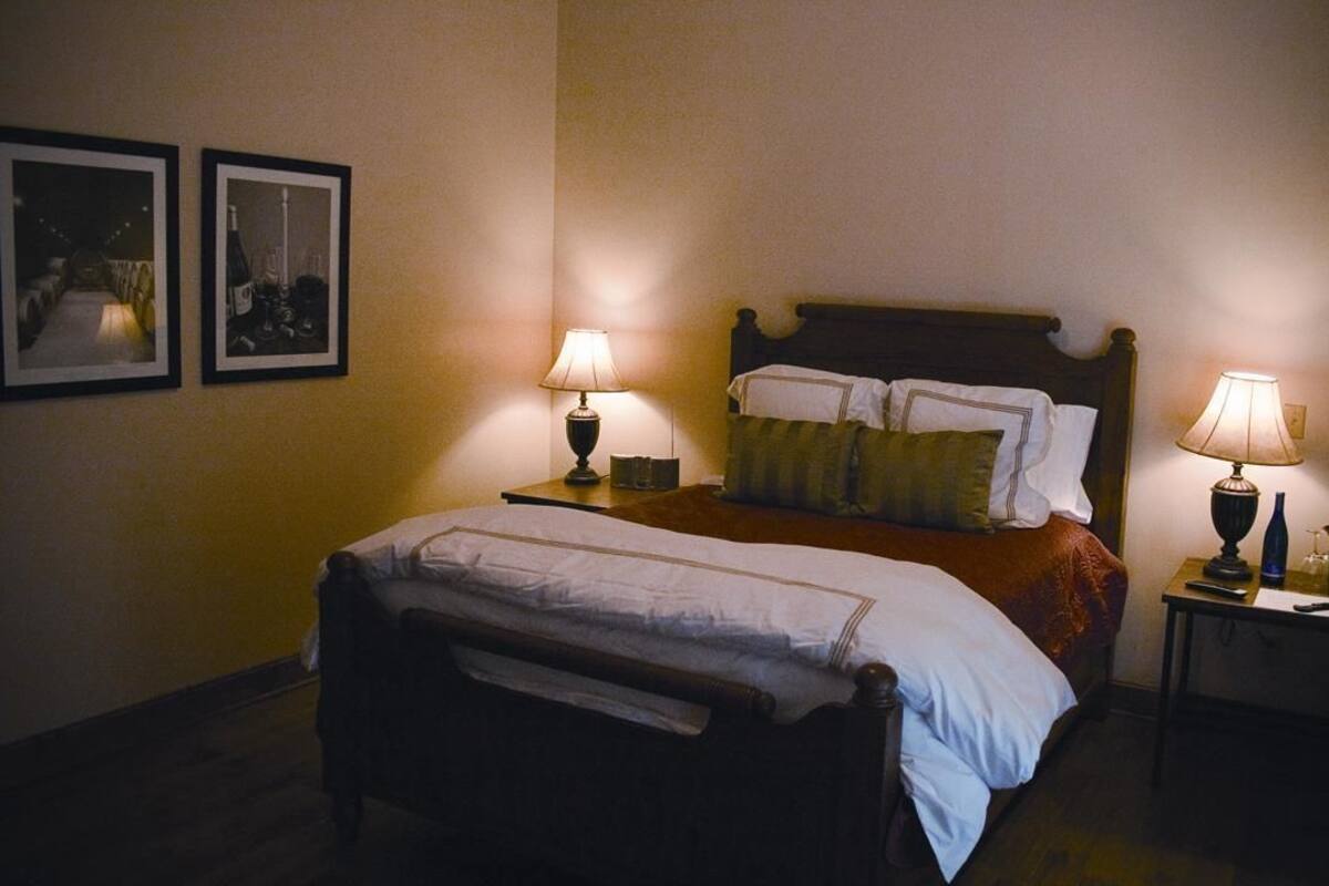 A hotel room with a double bed, two bedside tables with lamps, a headboard, and two framed pictures on the wall.