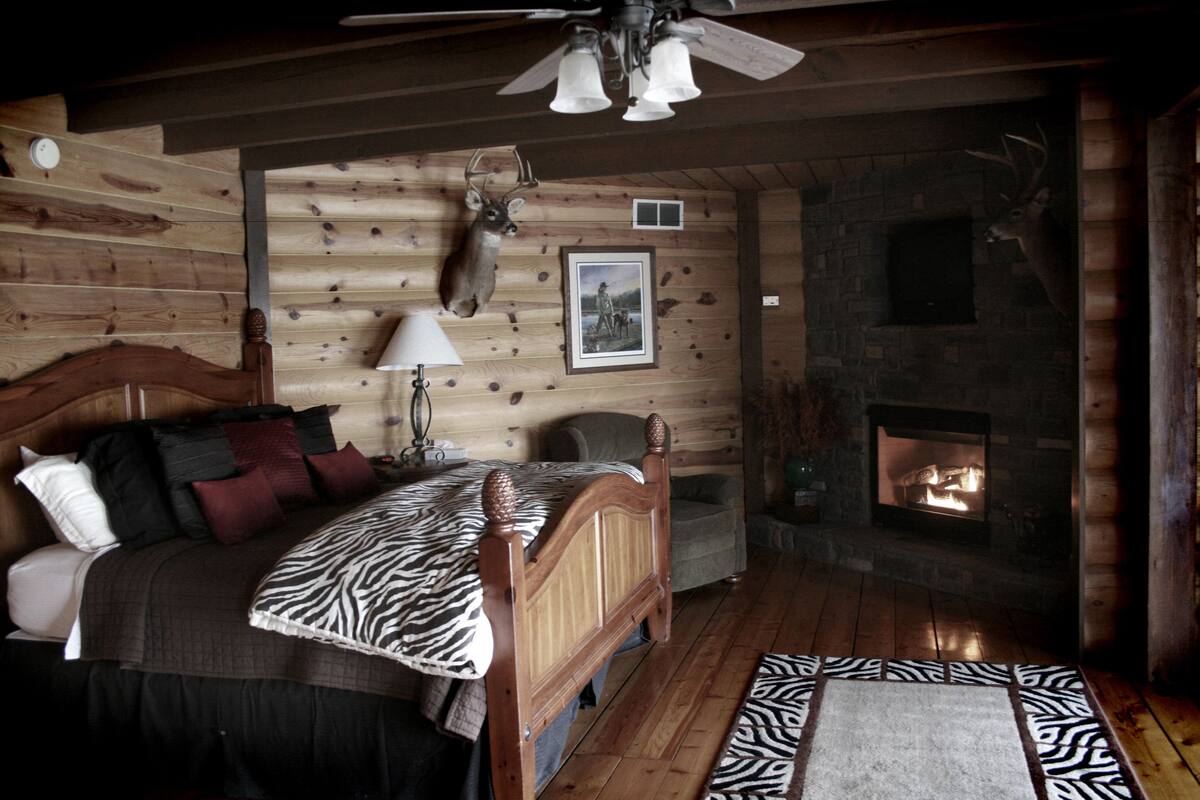 A log cabin bedroom with a bed, a fireplace, and mounted animal heads on the wall.