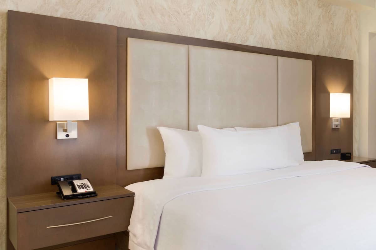 A hotel room with a large bed, two bedside lamps, a nightstand with a telephone, and a wall-mounted panel.