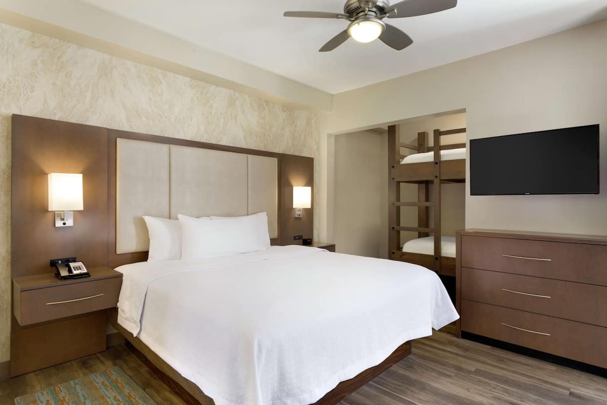 A hotel room with a large bed, bedside lamps, a TV, a wardrobe, and a ceiling fan.