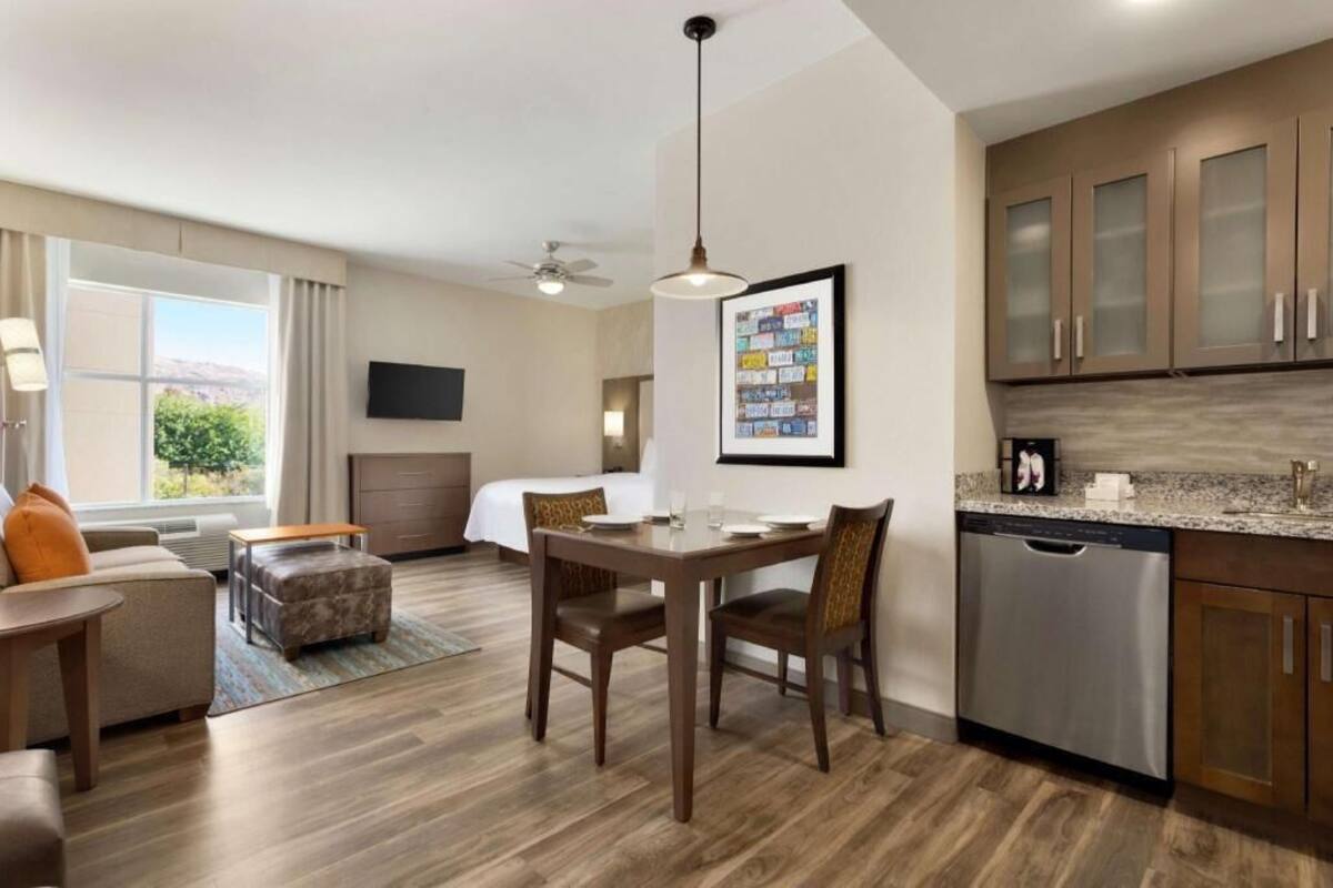 A hotel room with a dining area, kitchenette, and a bed.