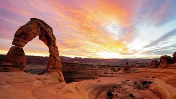 A natural rock formation arching over a desert landscape at sunset.