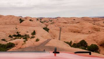 A red vehicle on a winding road through a rocky landscape with sparse vegetation.
