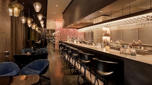 Un espace bar moderne doté d’un long comptoir, de tabourets de bar et de luminaires suspendus.