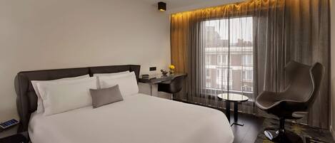 A hotel room with a large bed, a bedside table with a phone, a chair, and a window with curtains.