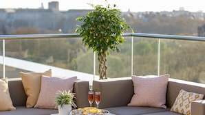 Un balcon avec un ensemble de meubles de salon, une table avec un saladier de fruits et des boissons, et une plante en pot.