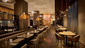Un restaurant moderne avec des banquettes en cuir, des tables rondes et des luminaires suspendus.