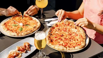 Two pizzas on plates, a glass of beer, and a glass of orange juice on a table.