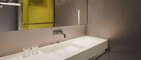 A modern bathroom with a white sink, a large mirror, and a yellow accent wall.