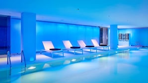Une piscine intérieure moderne, dotée d’un éclairage bleu, de chaises longues et d’un espace piscine dégagé.