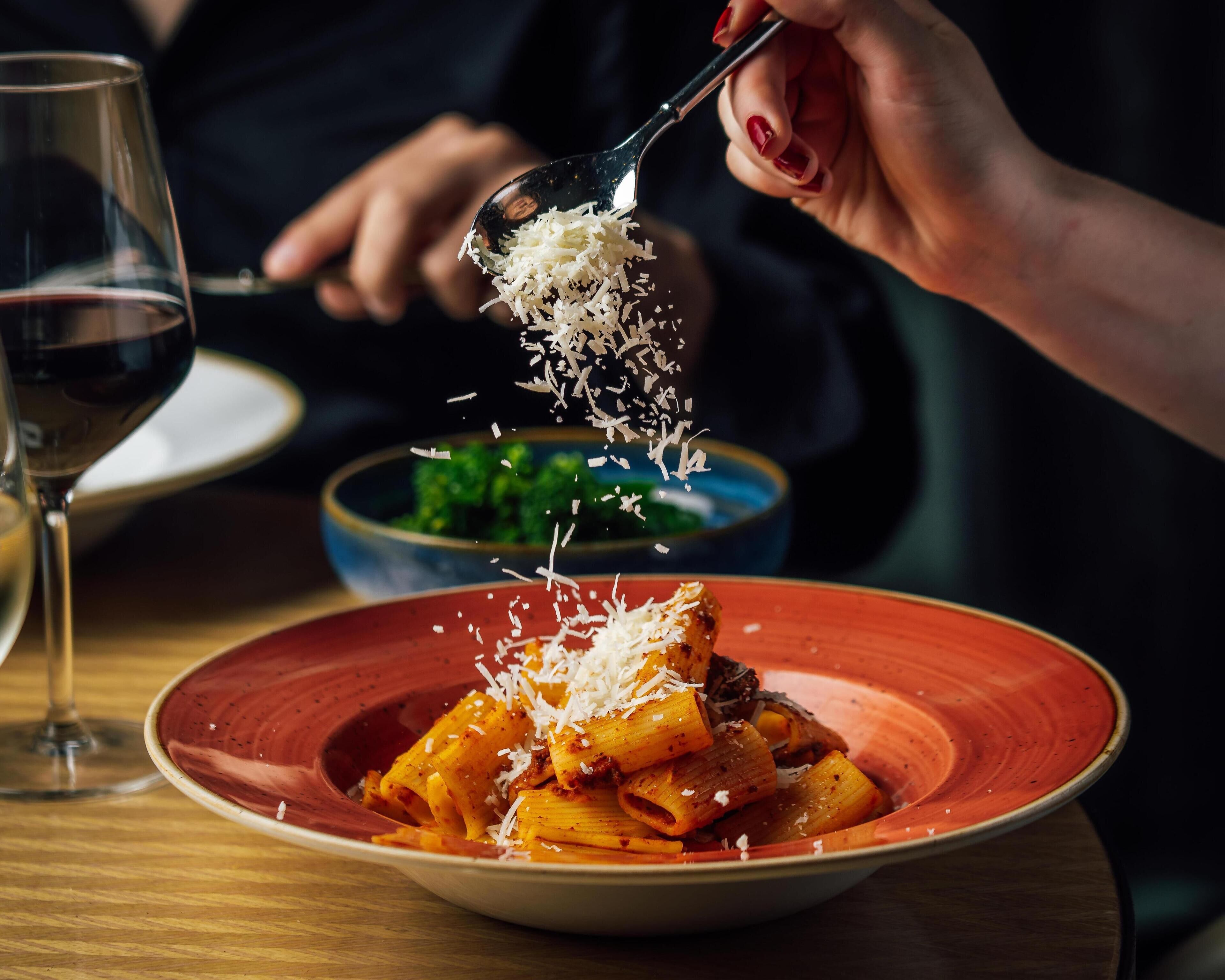 Una persona sirviendo pasta con queso rallado.