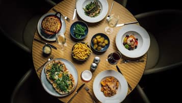 A round dining table with various dishes including pizza, pasta, and a dessert, surrounded by chairs.