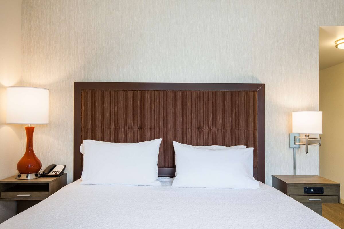 A hotel room with a large bed, two bedside tables, a telephone, and a lamp on each side.