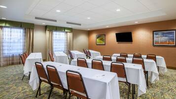 A conference room with tables and chairs, a flat-screen TV on the wall, and a window with curtains.