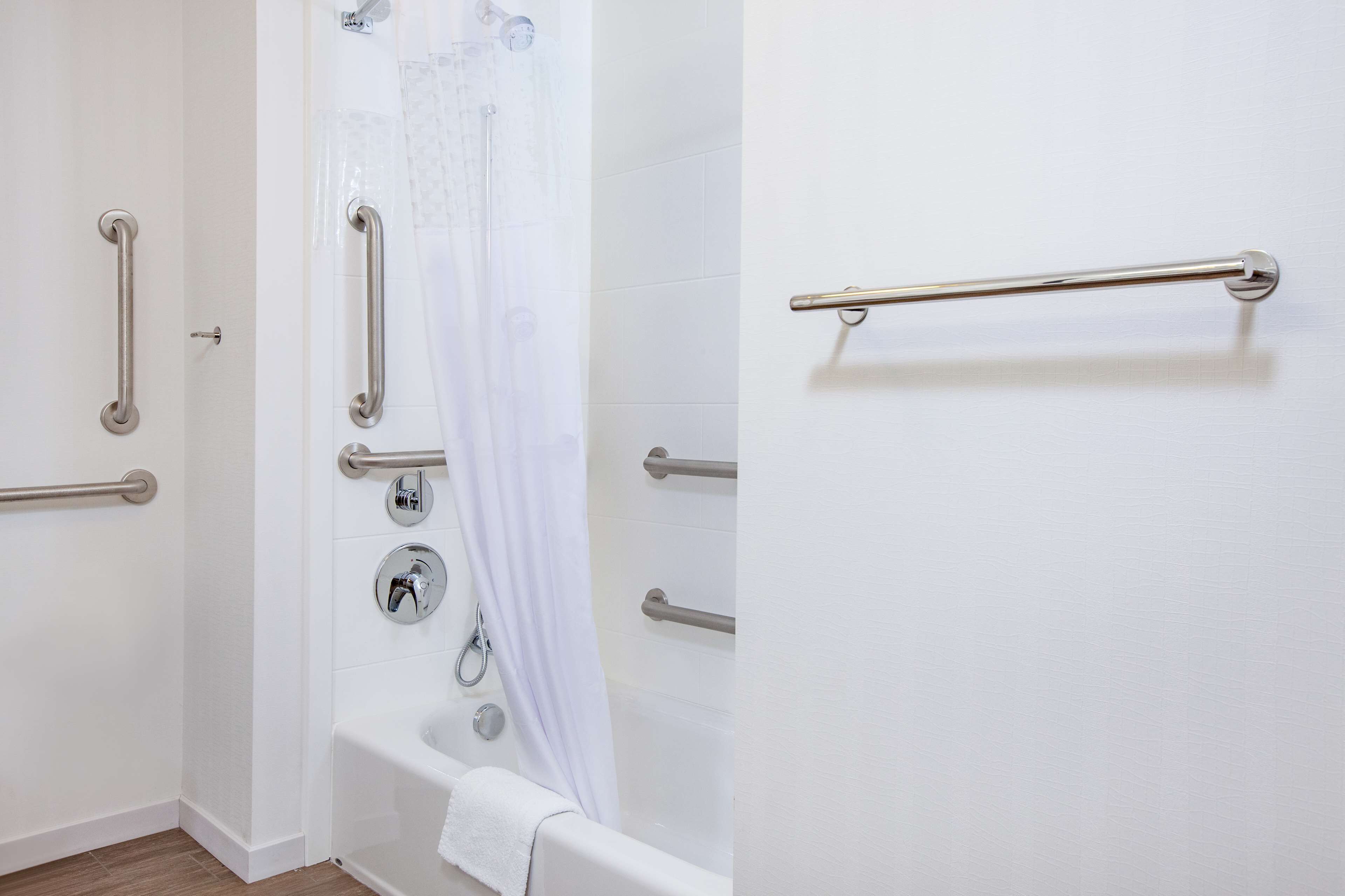 A bathroom with white walls, a bathtub, and multiple handrails.