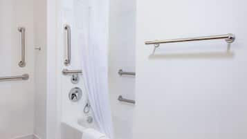 Un baño con paredes blancas, una bañera y varios pasamanos.