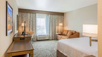 A hotel room with a bed, a desk, a chair, a sofa, and a window with curtains.