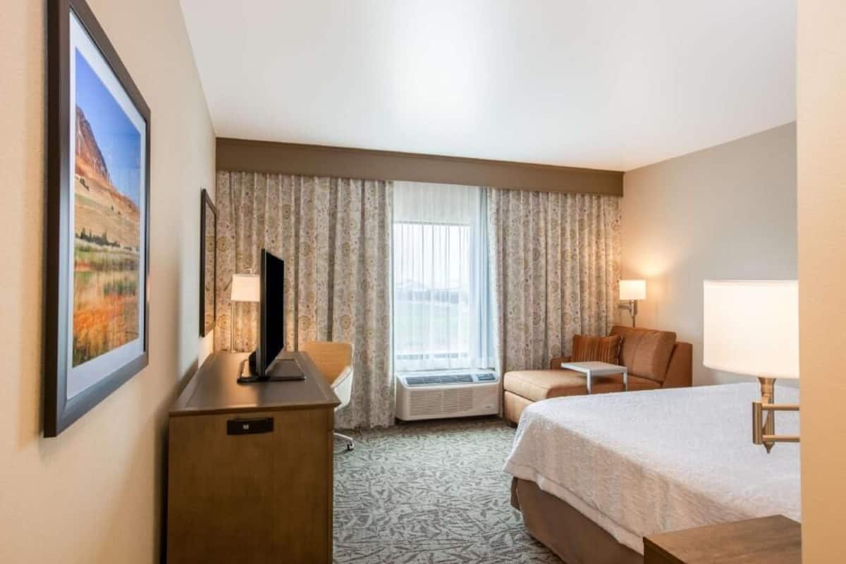 A hotel room with a bed, a desk, a chair, a TV, a lamp, and a window with curtains.