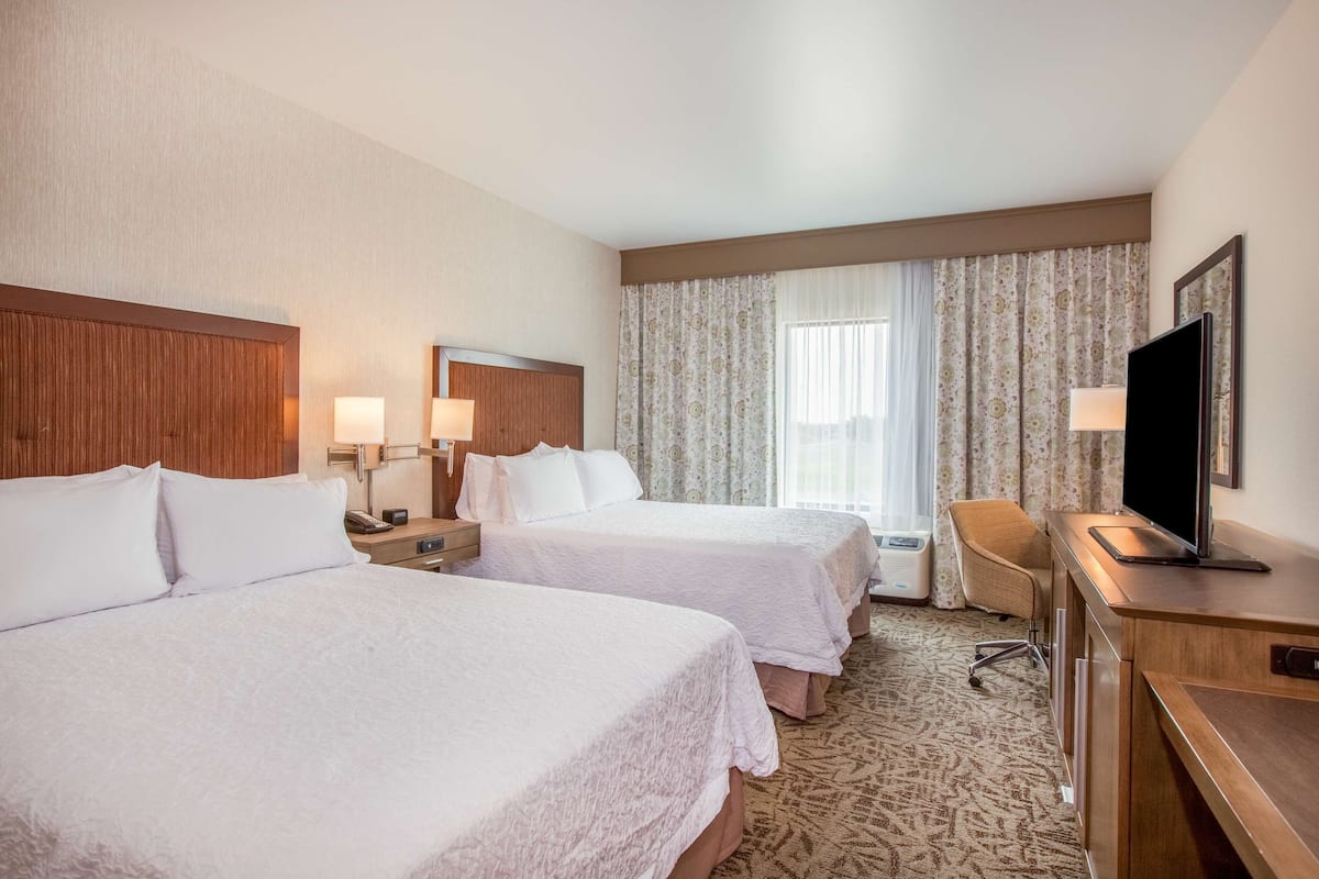 A hotel room with two beds, a desk, a chair, a TV, and a window with curtains.