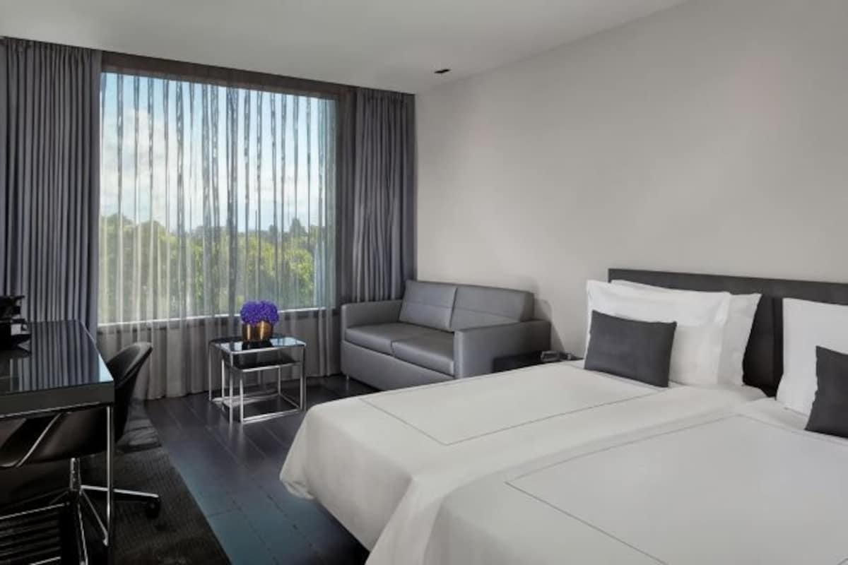 Habitación de hotel con una cama grande, un sofá, un escritorio y vistas al exterior a través de amplias ventanas.