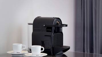 A black espresso machine with a glass carafe and two white cups on saucers.