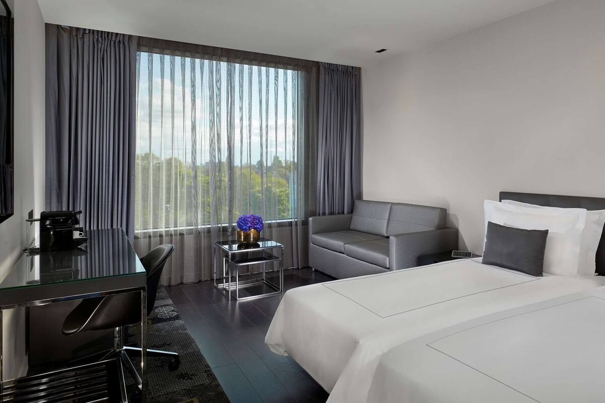 A hotel room with a bed, a desk, a sofa, and a view of the outdoors.