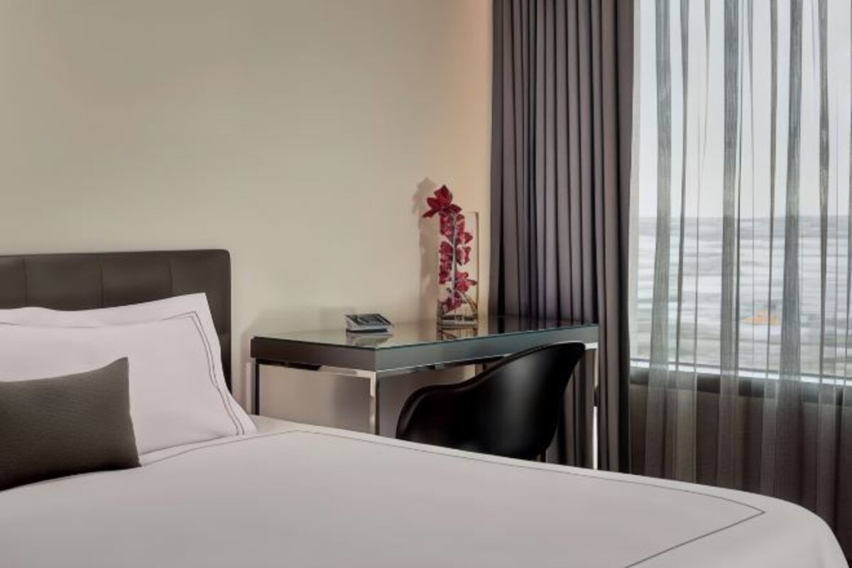 Une chambre d’hôtel avec un lit, un bureau, une chaise et une fenêtre avec des rideaux.