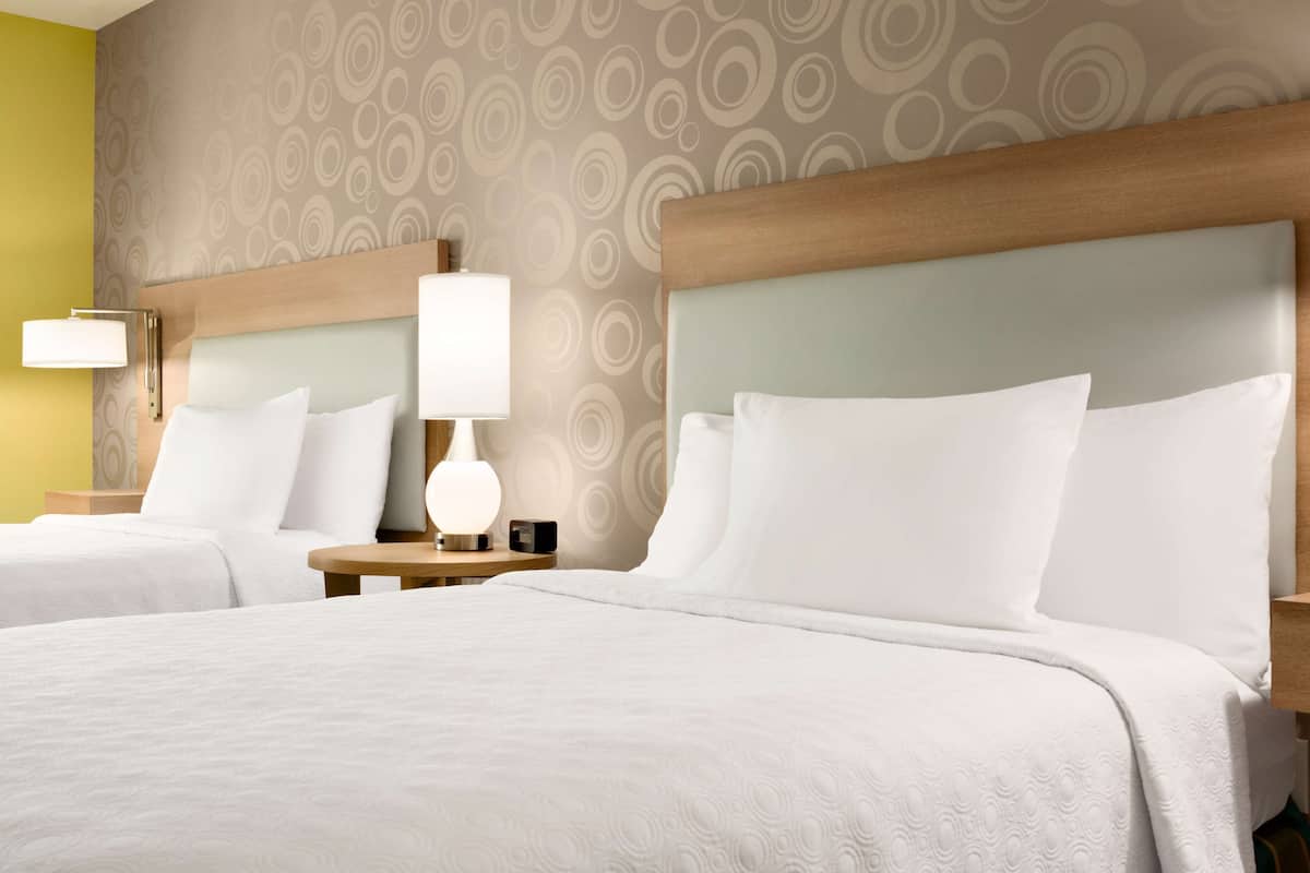 Hotelkamer met twee bedden, een nachtkastje met lamp en een muur met een rond patroon.