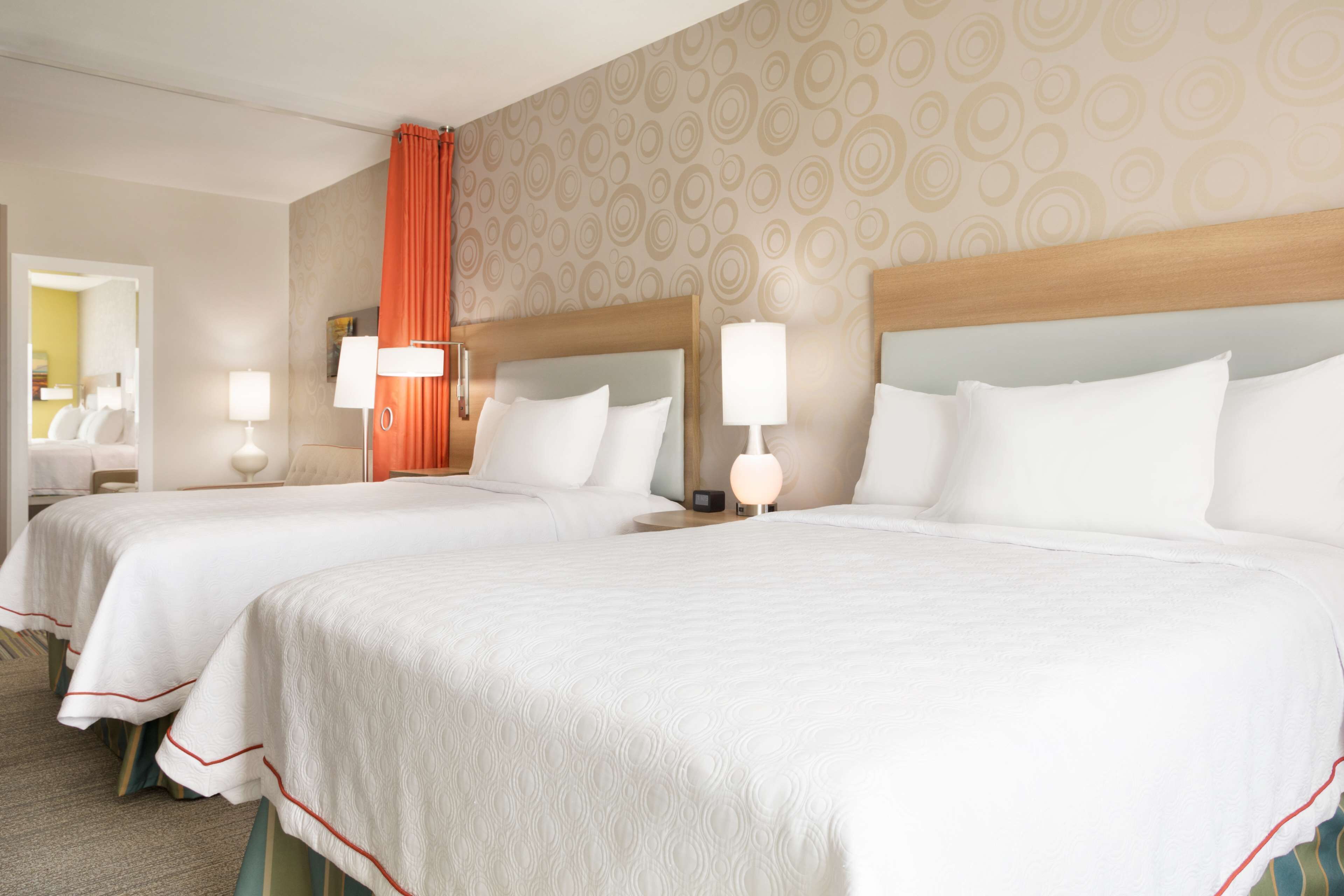 A hotel room with two beds, each with a headboard, bedside lamps, and a mirror.