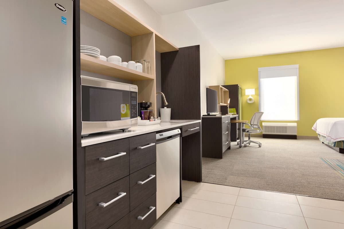 Een moderne hotelkamer met een keukenhoek, een bureau en een bed.