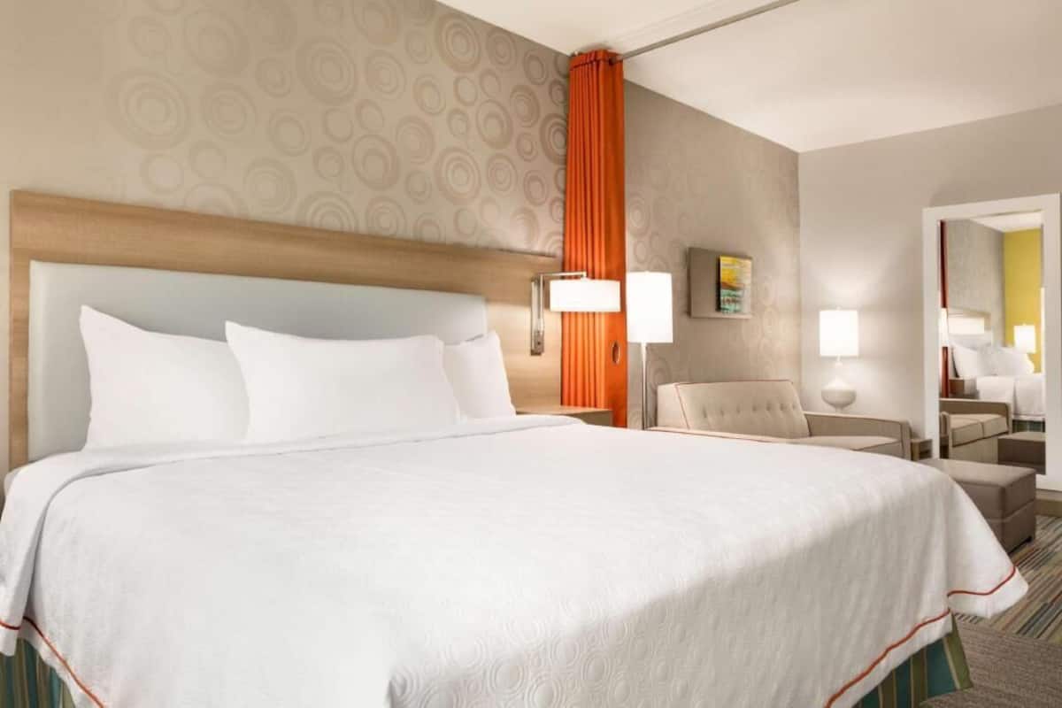 Een hotelkamer met een groot bed, een hoofdbord, een nachtkastje met een lamp, een stoel en een spiegel.