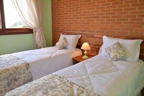 A room with two beds, a brick wall, and a window with curtains.