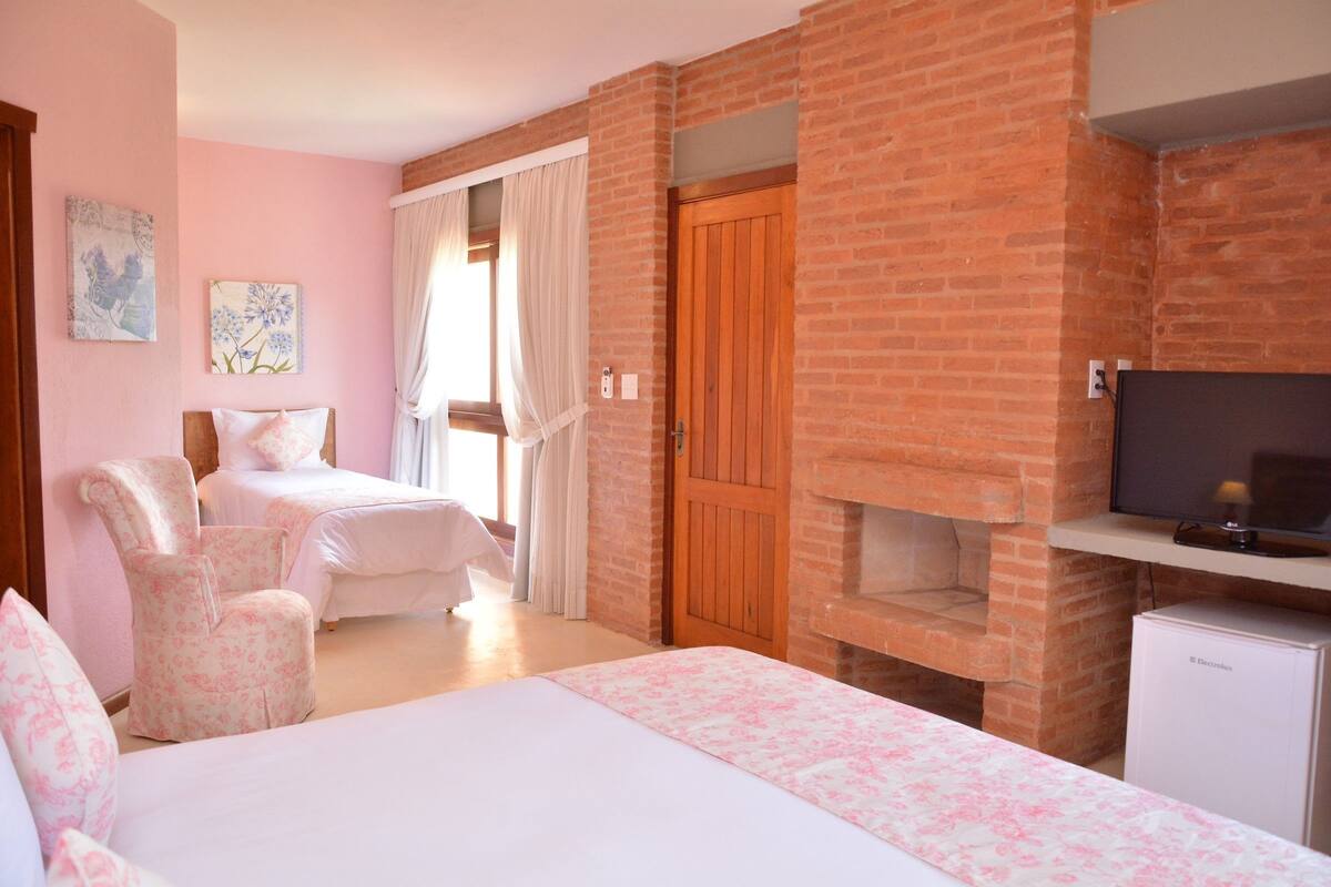A bedroom with two beds, a brick fireplace, a television, and a small refrigerator.