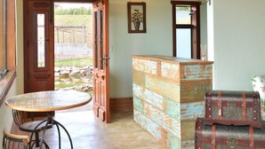 A rustic interior with a wooden ceiling, a round table with metal chairs, a wooden counter, and a vintage suitcase. - Pousada Villa dos Leais (Serra Negra)