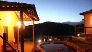 A building with a covered patio, a small pond, and a wooden bench. - Pousada Villa dos Leais (Serra Negra)