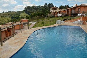 A swimming pool with a tiled deck, white lounge chairs, and umbrellas.