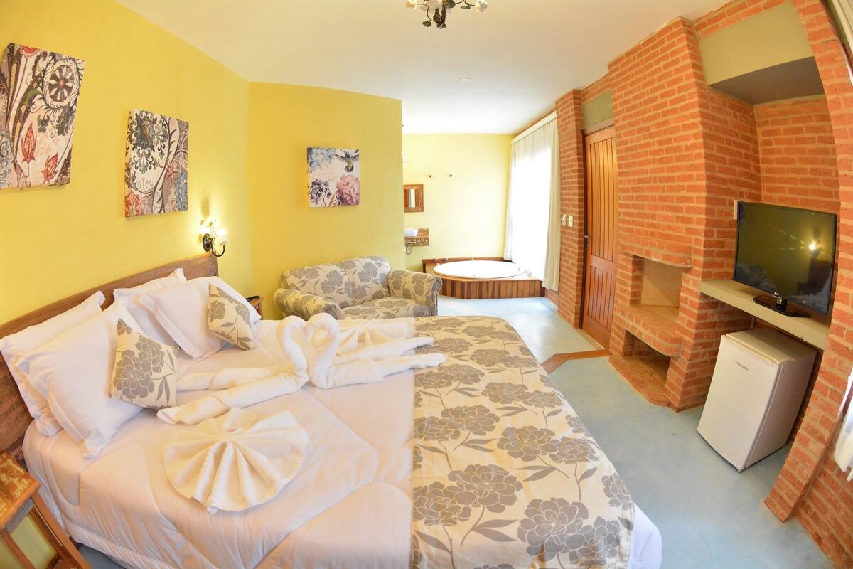 A hotel room with a bed, a sofa, a small table, a TV, and a brick fireplace.