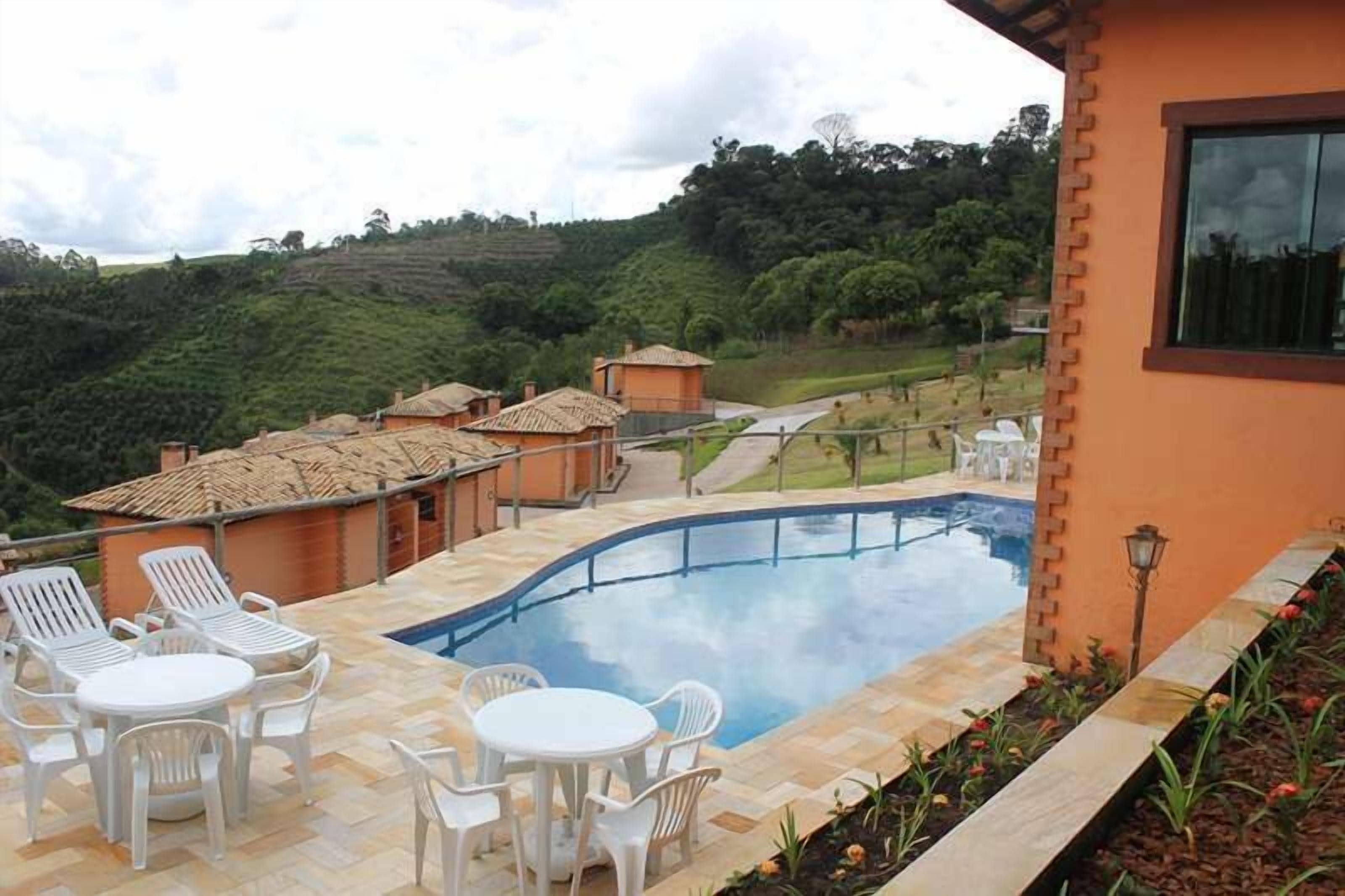 Área de piscina com espreguiçadeiras e uma mesa, rodeada por um edifício de tijolos com telhado telhado.