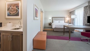 A hotel room with a bed, desk, and a small kitchenette.