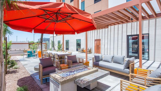 An outdoor seating area with a fire feature, wooden furniture, and a large red umbrella.