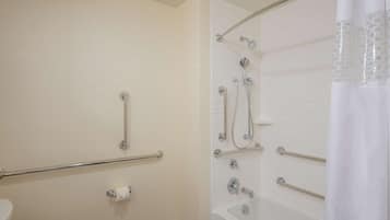 Un baño con inodoro, barras de apoyo, ducha con cabezal de ducha manual y bañera.