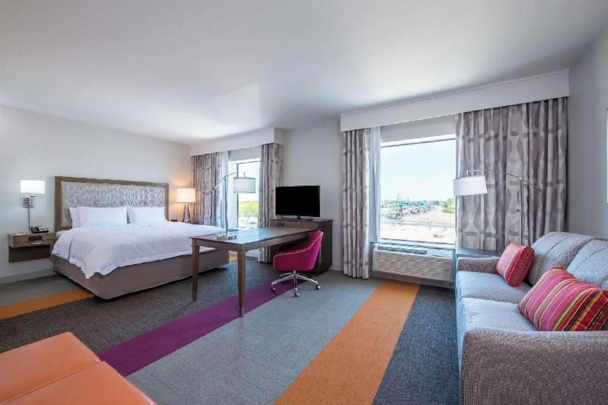 Quarto de hotel com cama, escrivaninha, televisão e sofá.