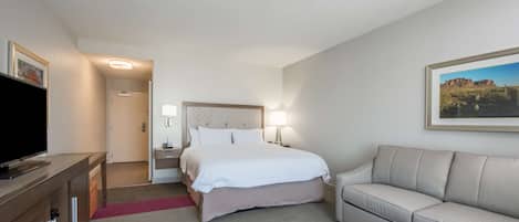 A hotel room with a bed, a TV, a sofa, and a painting on the wall.