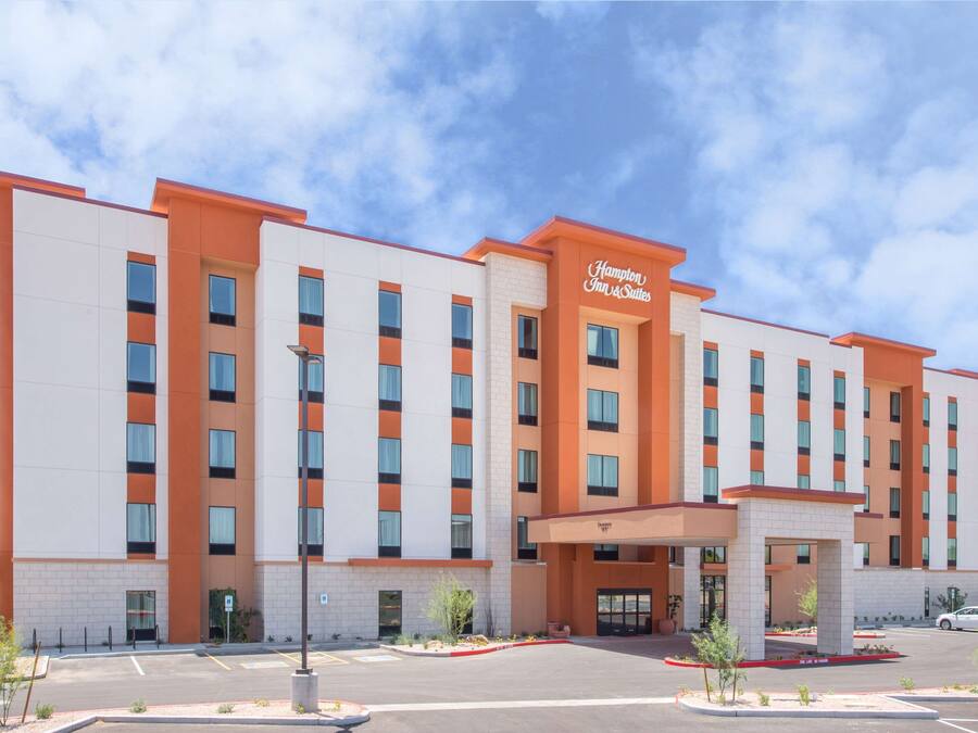Un hotel de varios pisos con un diseño moderno, que destaca un cartel llamativo de Hampton Inn & Suites.
