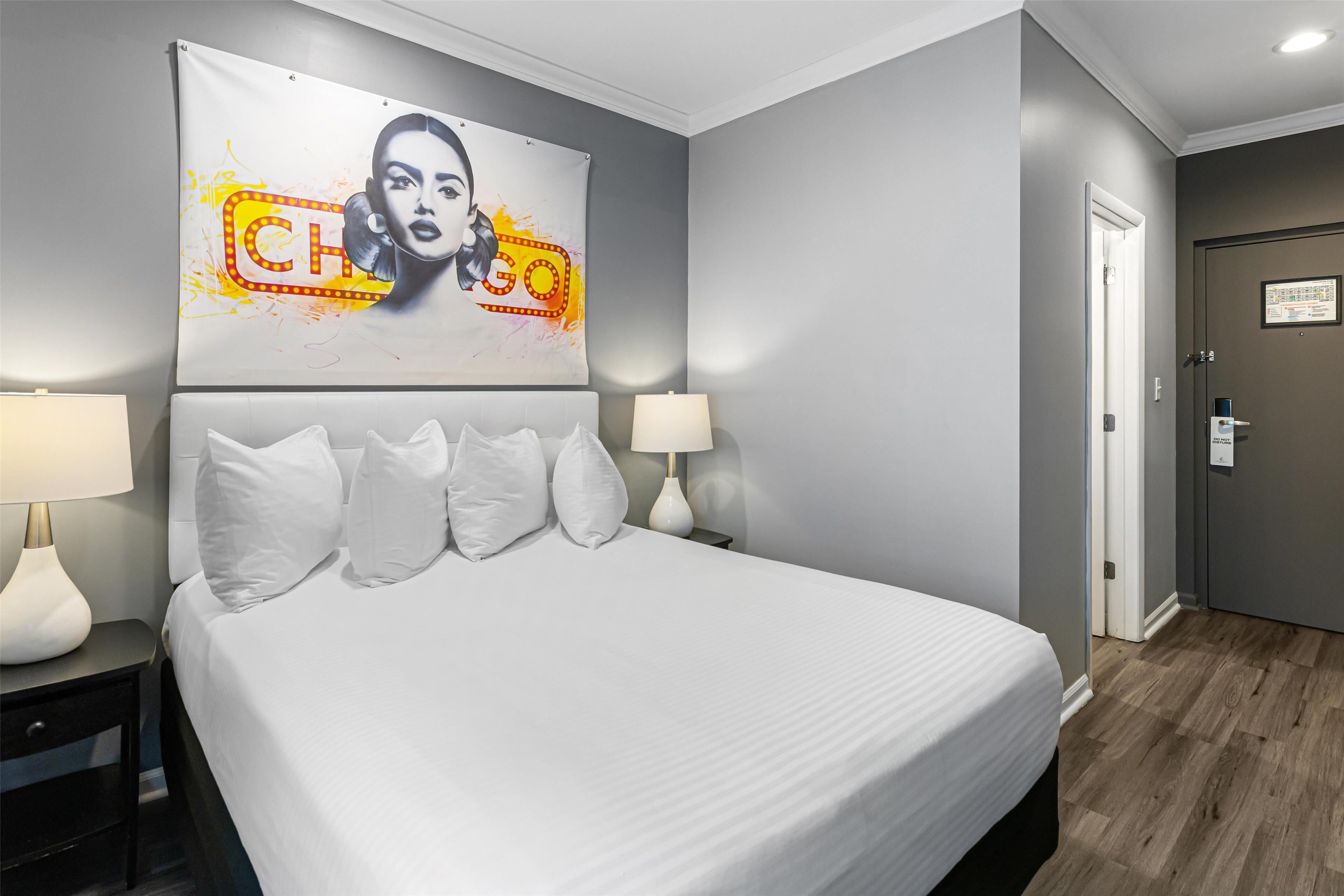 A hotel room with a large bed, two bedside tables with lamps, a wall-mounted artwork, and a door with a lock.