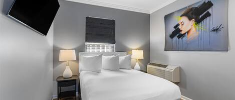 Un dormitorio moderno con cama, mesitas de noche con lámparas, ventilador de techo, televisor montado en la pared y una obra de arte grande.