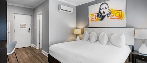 A hotel room with a large bed, a desk, a chair, and a wall-mounted air conditioner.