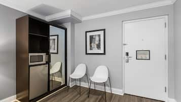 A compact room with a built-in microwave, two white chairs, a door with a notice, and a framed picture on the wall.