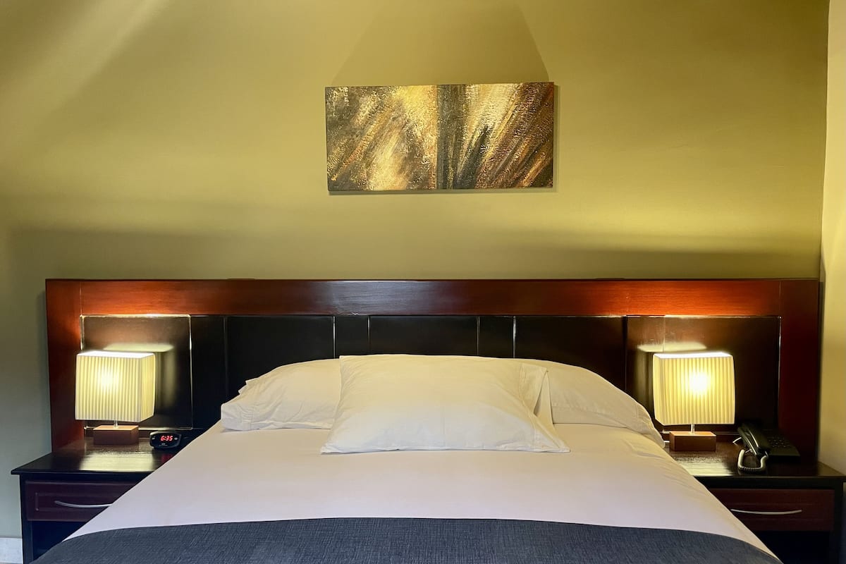 Un lit bien fait, avec une tête de lit en bois, deux lampes de chevet, une horloge et un tableau accroché au mur.
