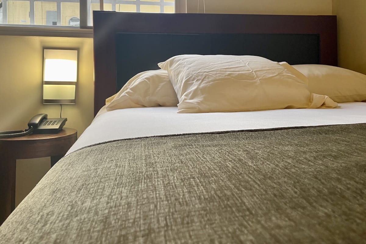 Une chambre d’hôtel avec un lit bien fait, un téléphone sur la table de chevet et une lampe sur une petite table à côté du lit.